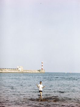 A woman standing in shallow water near a lighthouse on a sunny day.