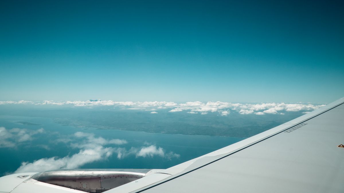 A stunning view from an airplane wing capturing the vast ocean and scattered clouds below.