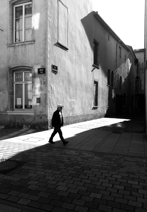 A man walking down a narrow alley in black and white