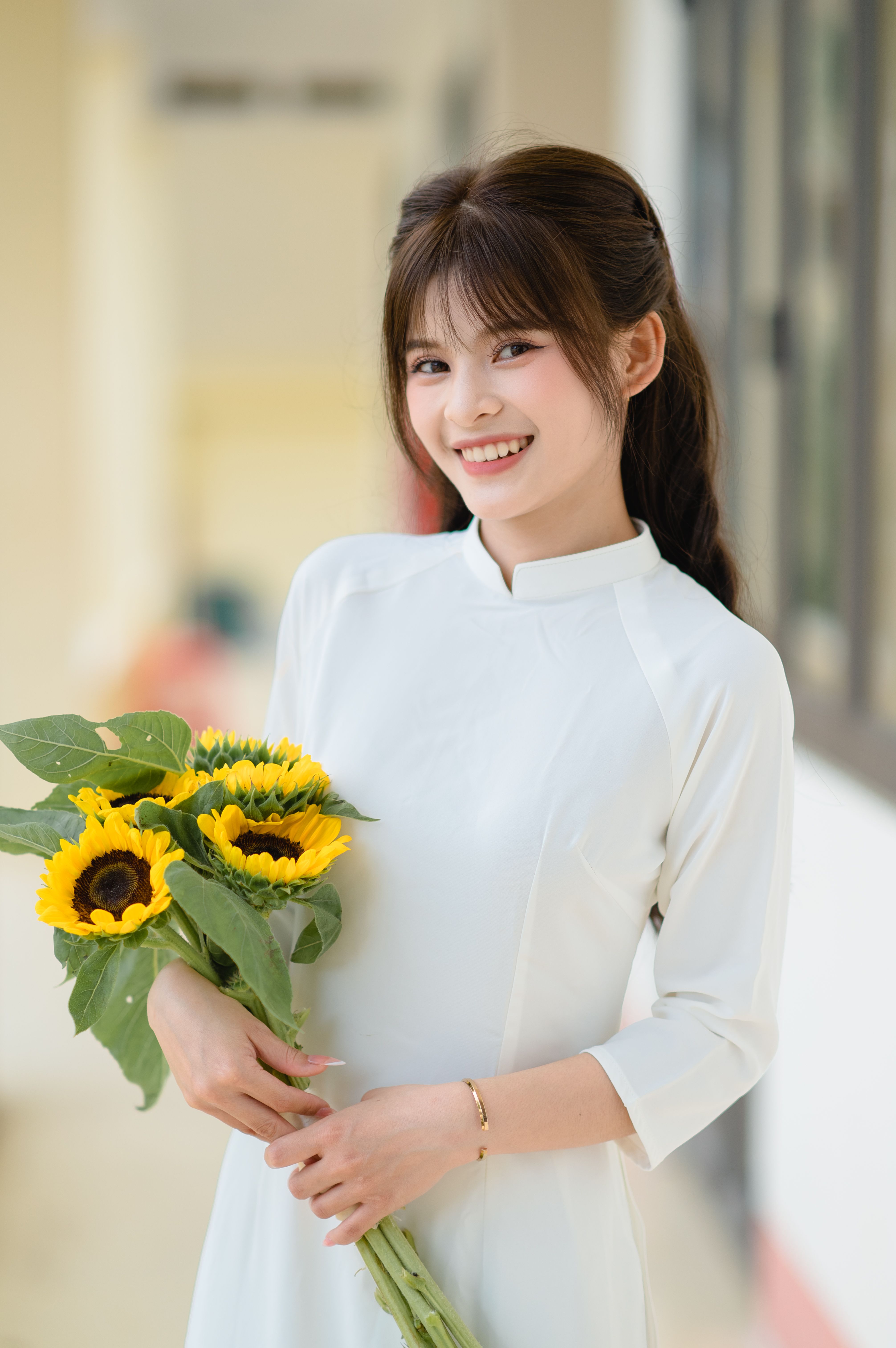 A smiling woman in a white ao dai holds sunflowers, captured in Lang Son, Vietnam.