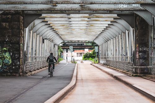 Free A lone cyclist rides through a steel bridge on a city street with graffiti-covered walls. Stock Photo