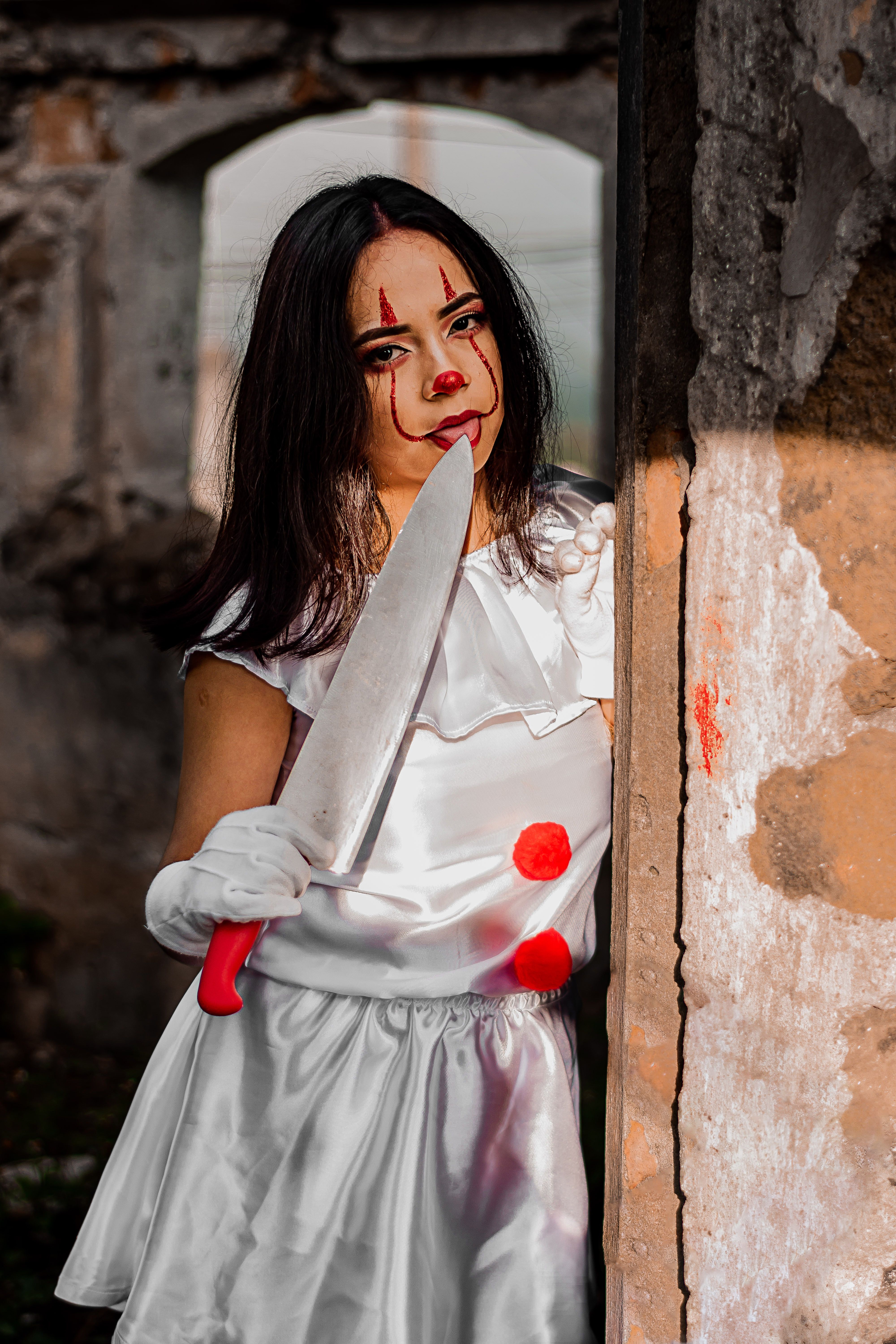Woman in clown costume holding a knife, posing dramatically outdoors.