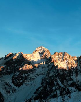 Breathtaking view of snow-capped mountains in Almaty, Kazakhstan, beautifully illuminated by sunset's warm glow.