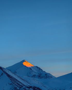 Stunning view of a snow-covered mountain peak illuminated by sunrise in Almaty, Kazakhstan.