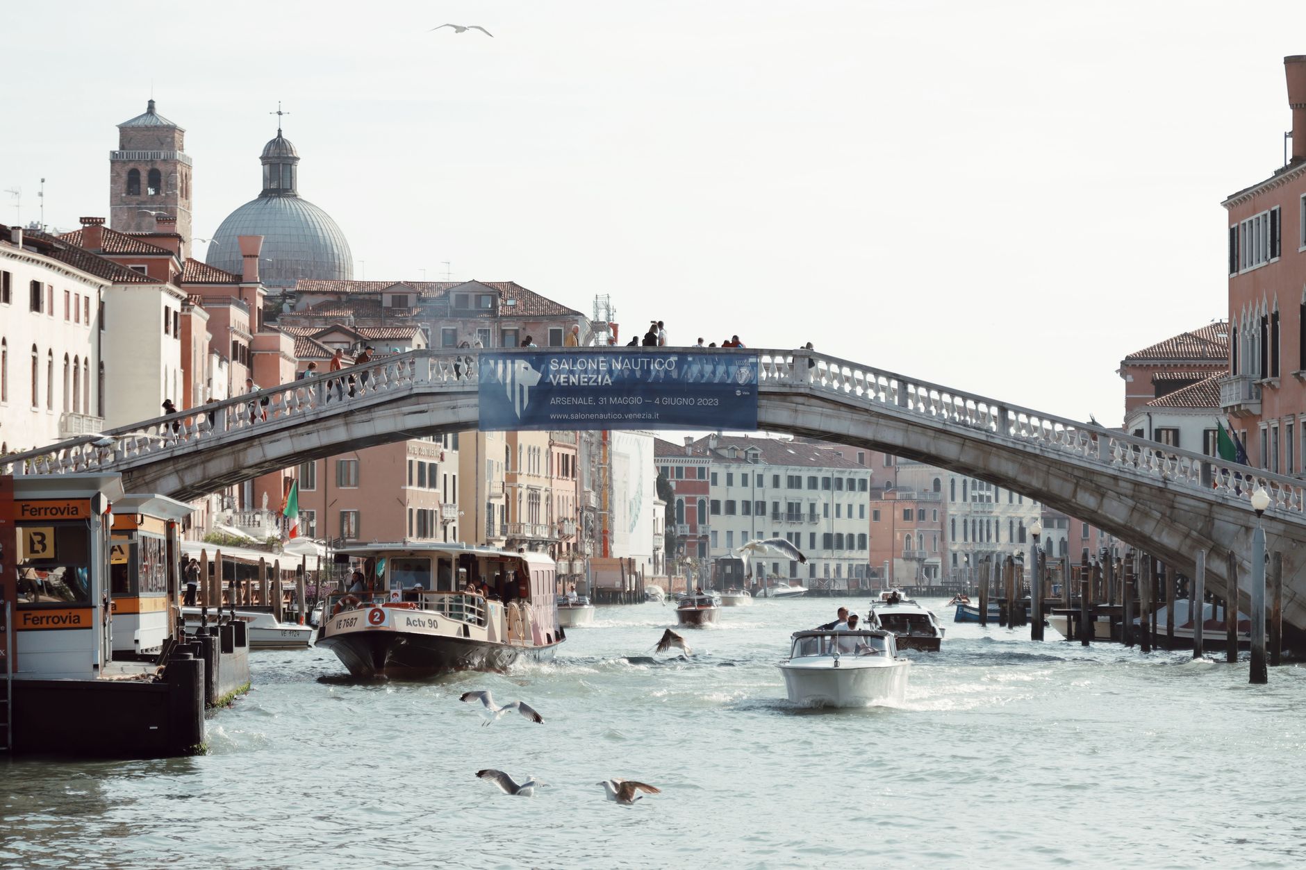 Scenic view of boats navigating a Venetian canal under a classic stone bridge, Venice, Italy.