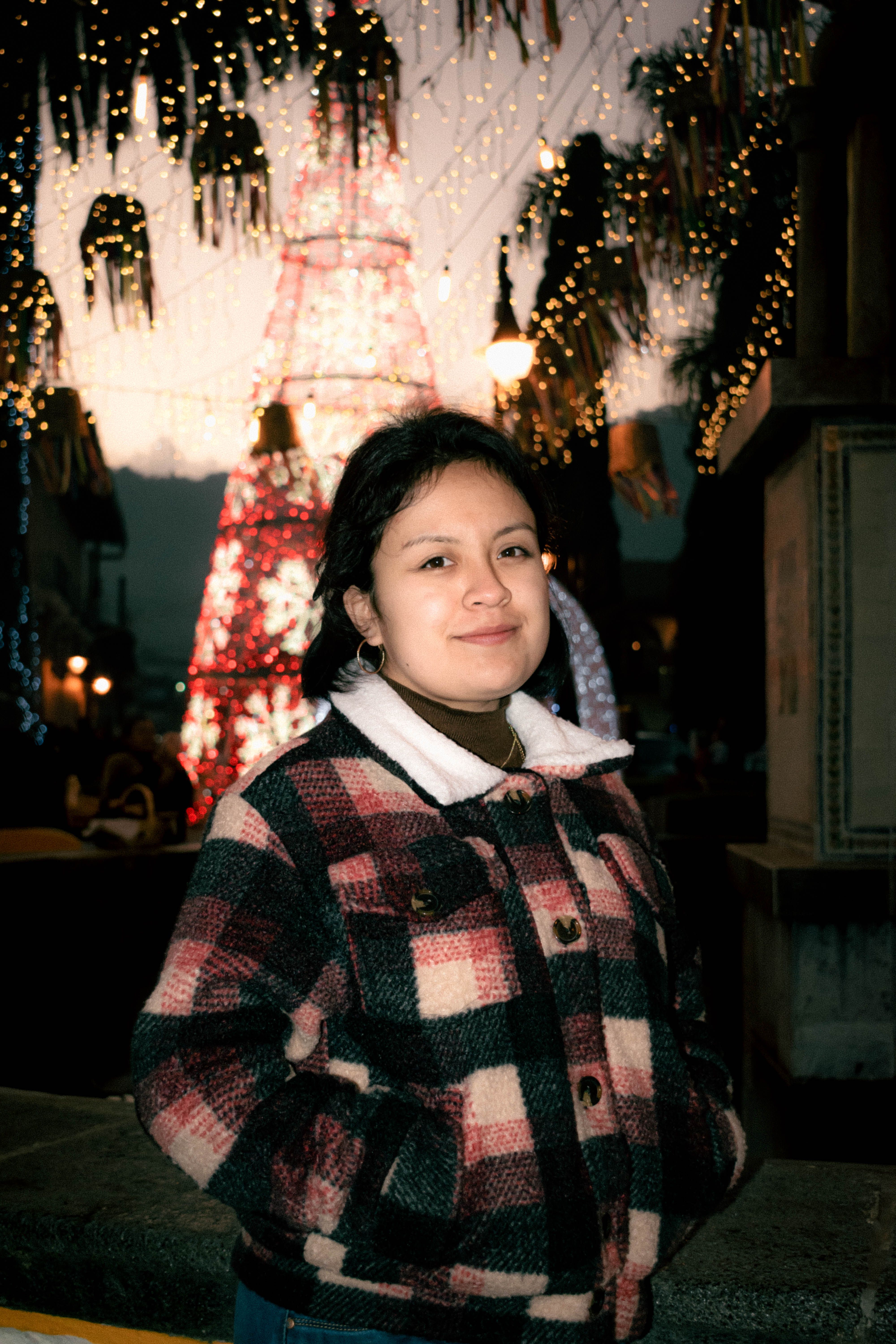 A woman stands confidently amidst festive lights in Ciudad de Tlatlauquitepec, Puebla, Mexico.
