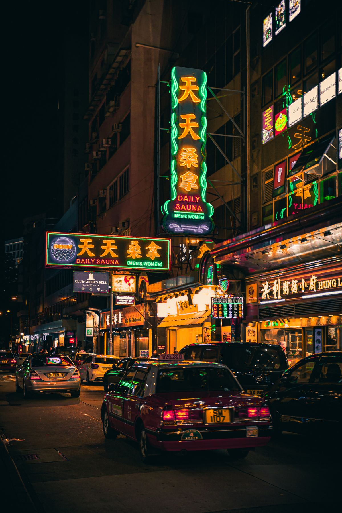 Red taxi on a busy Hong Kong road at night beside illuminated buildings
