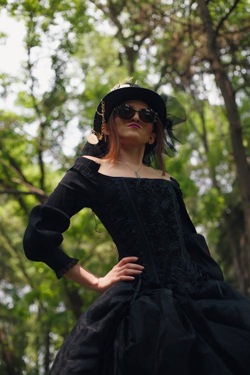 A woman in a black dress and hat posing in the woods