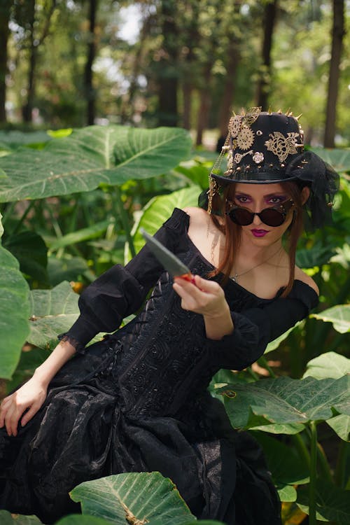 A woman in a black dress and hat is holding a cell phone