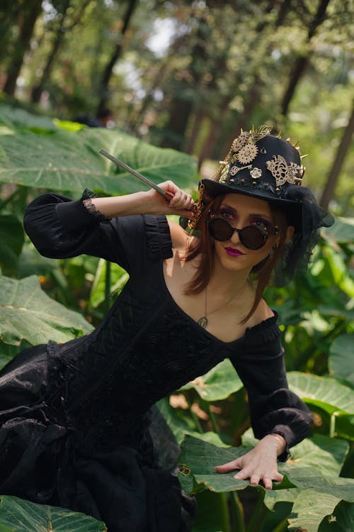 A woman in a black dress and hat posing in the jungle