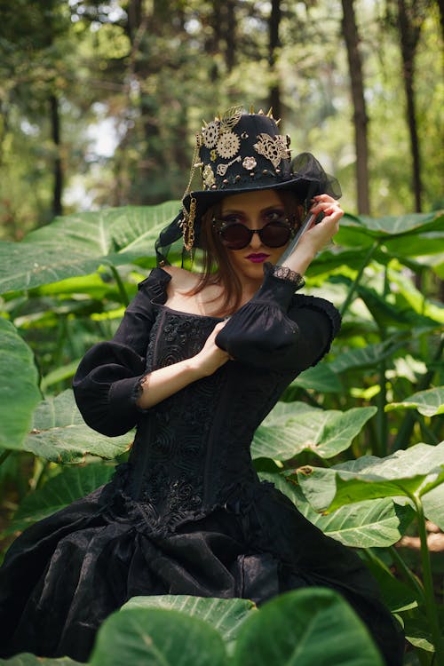 A woman in a black dress and hat is posing in the jungle