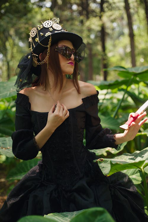 A woman in a black dress and hat is standing in the woods
