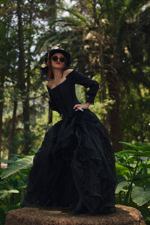 A woman in a black dress and hat standing in the woods