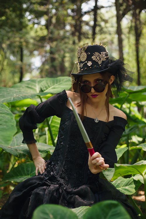 A woman in a black dress holding a knife in the woods