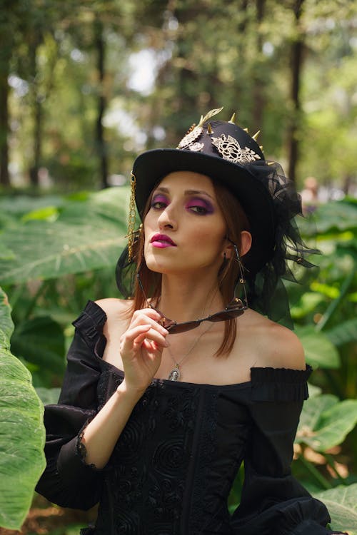 A woman in a black hat and dress posing in the woods
