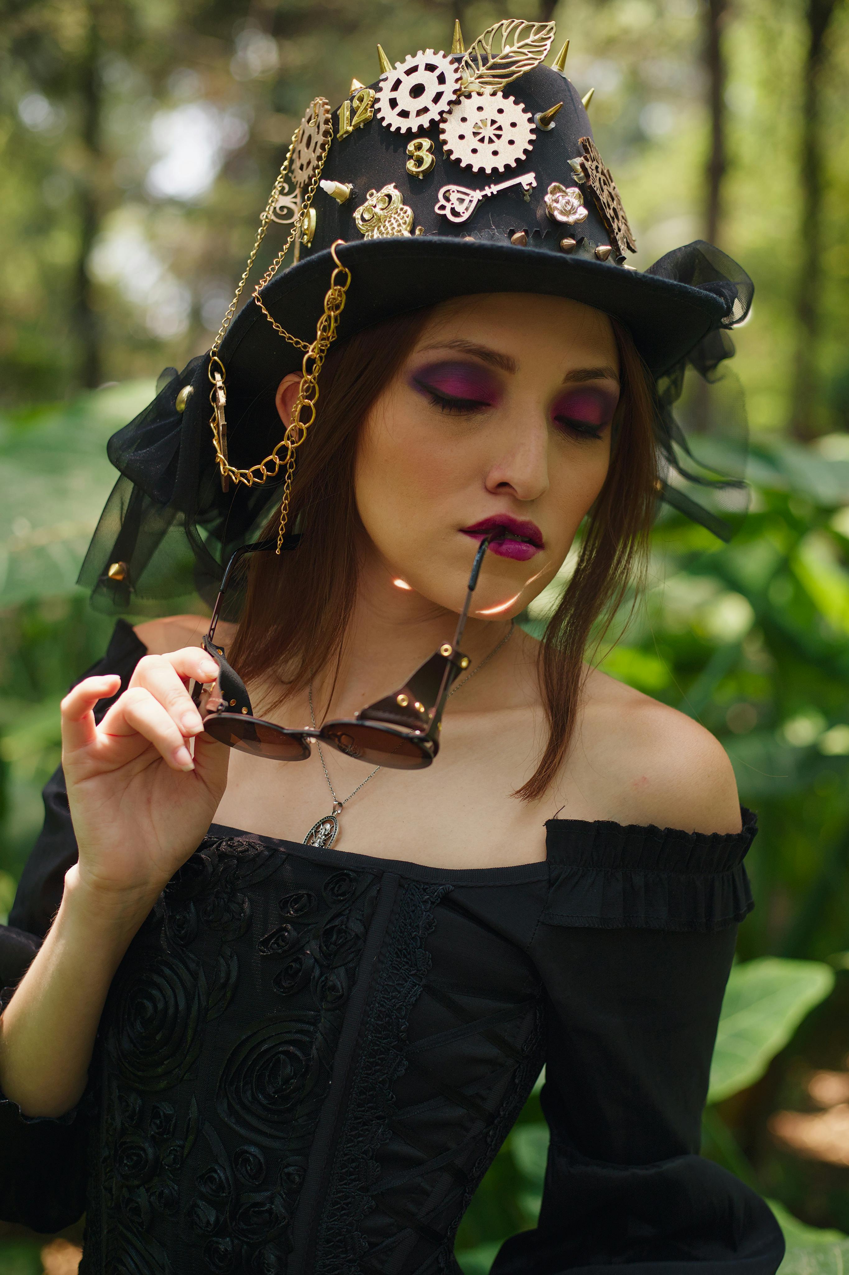 A fashionable steampunk model posing with sunglasses in a lush outdoor setting.