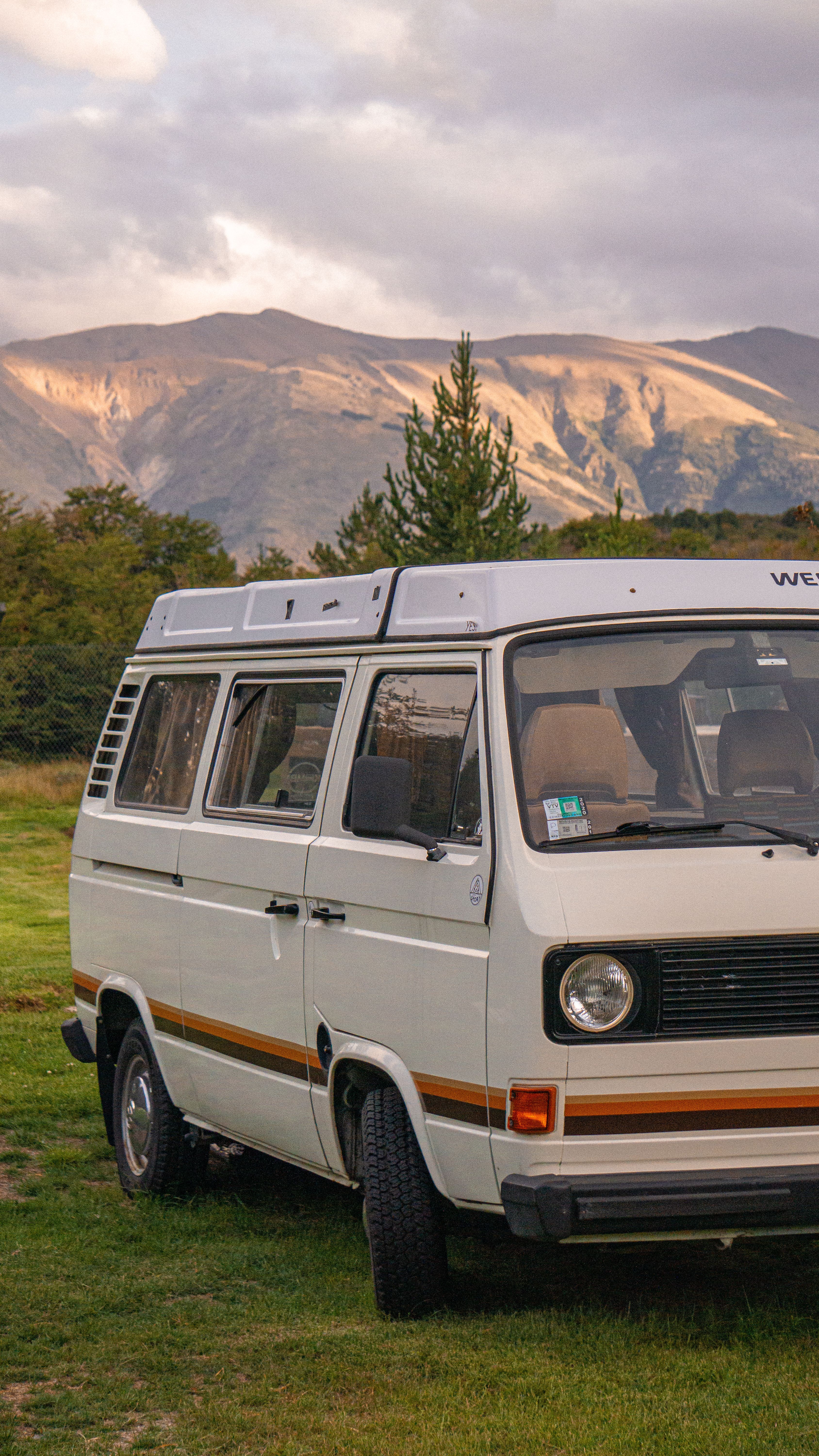 Vintage camper van parked against a stunning mountain backdrop during sunset, capturing a sense of adventure.