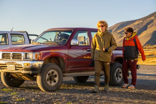 Two men standing by a red off-road truck in a sunny desert landscape.