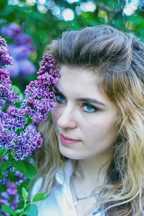 Free Portrait of a woman in a garden surrounded by lilac flowers with a serene expression. Stock Photo