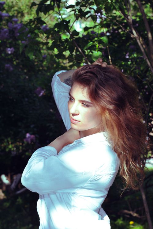Free A serene portrait of a young woman in a sunlit garden wearing a white shirt. Stock Photo