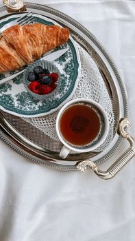 Stylish breakfast setup featuring a croissant, fresh berries, and tea on silver tray.