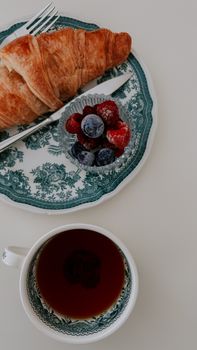 Top view of a breakfast setting with a croissant, berries, and coffee on elegant china.