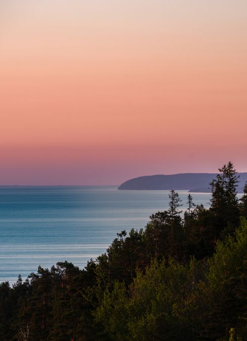 Free Stunning sunset over the Gränna coastline with a serene ocean view and lush forest foreground. Stock Photo