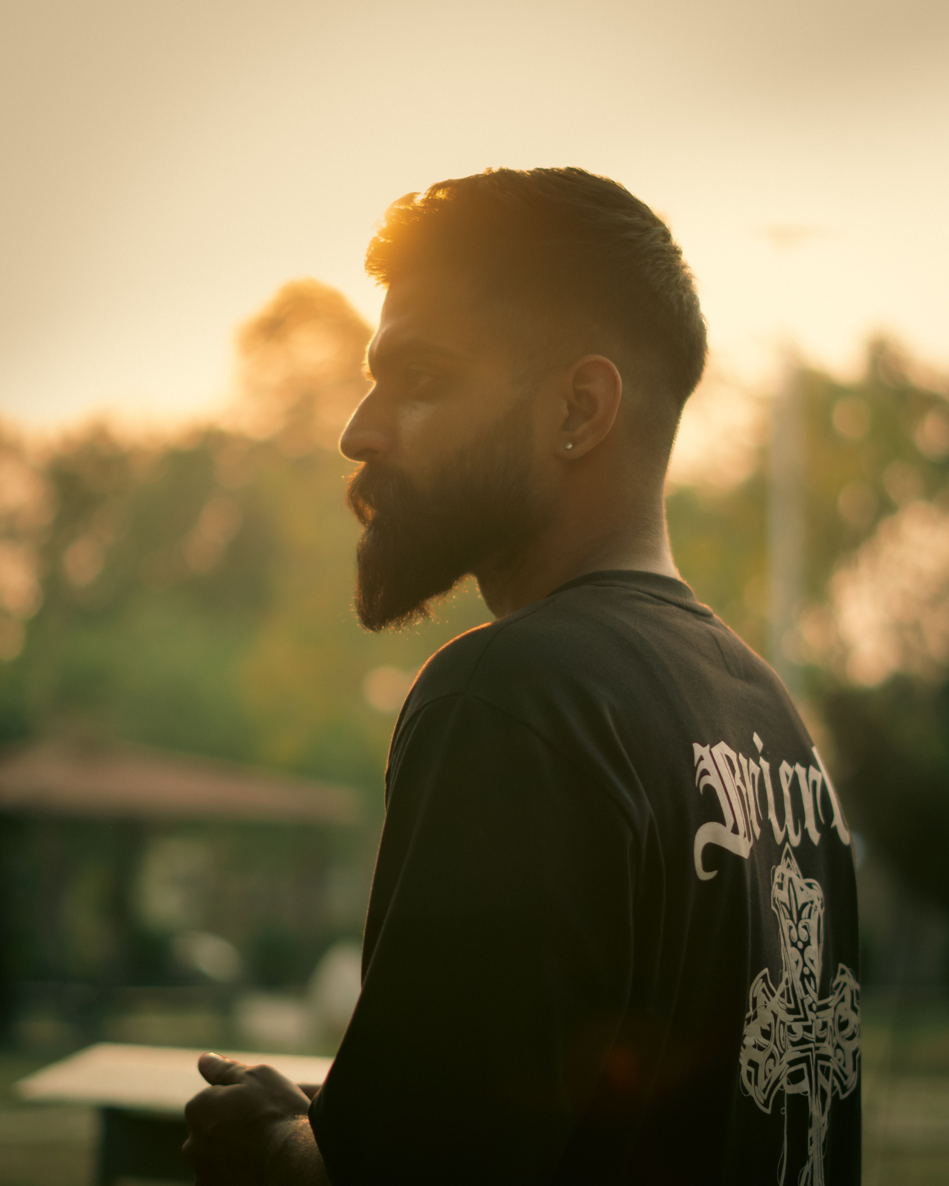 Bearded man in profile against a warm sunset background, captured in an outdoor setting.