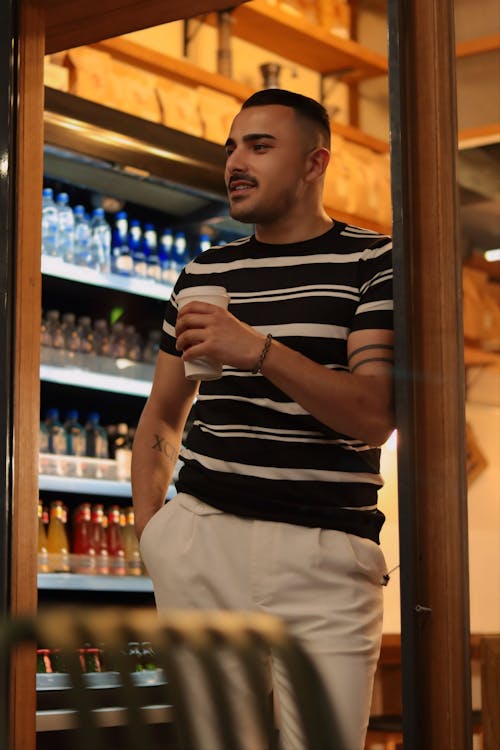 A man standing in front of a refrigerator holding a drink