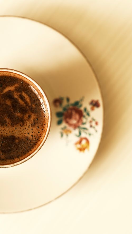 Free Vertical shot of a coffee cup on a floral saucer with rich frothy coffee. Stock Photo