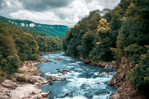 Free Explore a serene river meandering through lush green forests under cloud-filled skies. Stock Photo