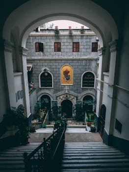 探索一座历史悠久的教堂庭院，穿过华丽的拱形入口，可见楼梯与郁郁葱葱的植物