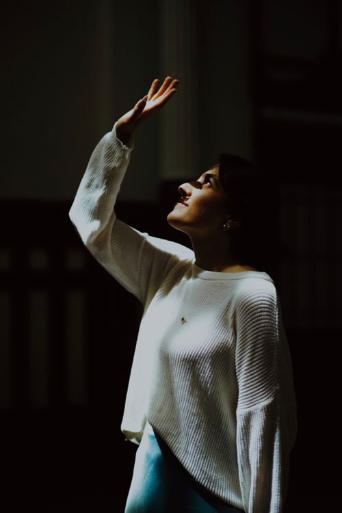 Free Side view of a woman looking up in dramatic indoor lighting, creating a serene moment. Stock Photo