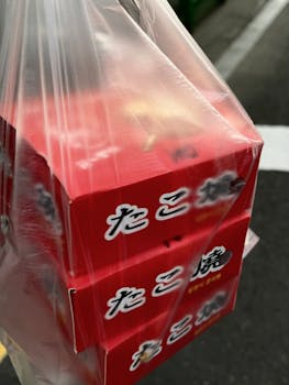Plastic bag holding red boxes of Takoyaki on the street in Sacheon, South Korea.