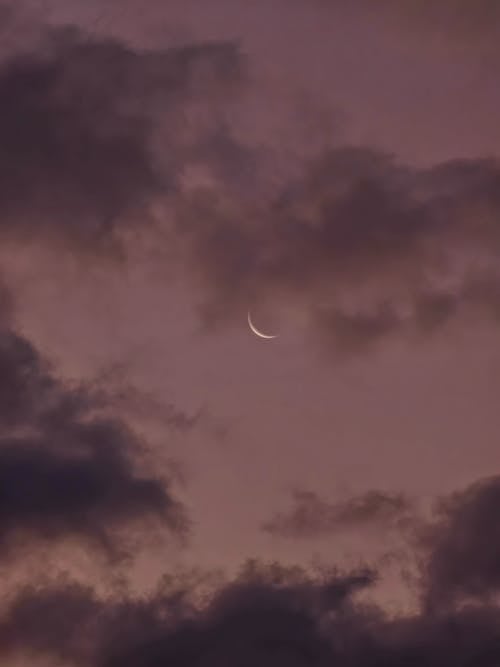 A crescent moon is seen through the clouds