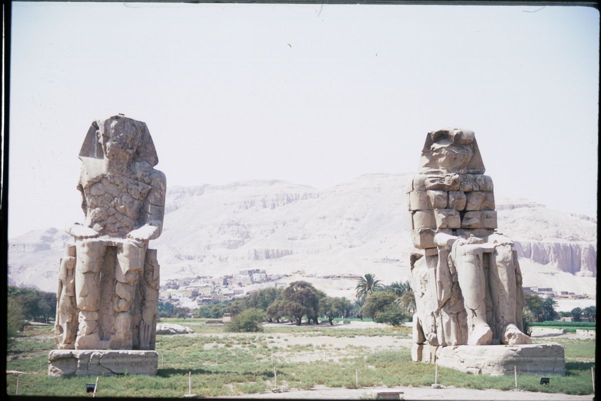 The two massive stone Colossi of Memnon statues standing in a field on Luxor West Bank