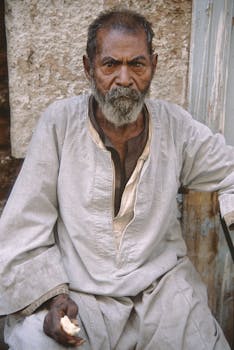 一位留着胡须的老人身着传统服装，摆好姿势拍照