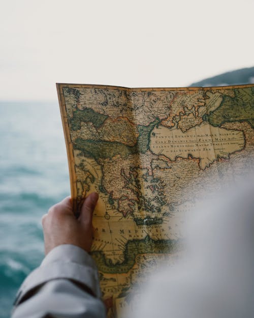 A person holding an old map in front of the ocean