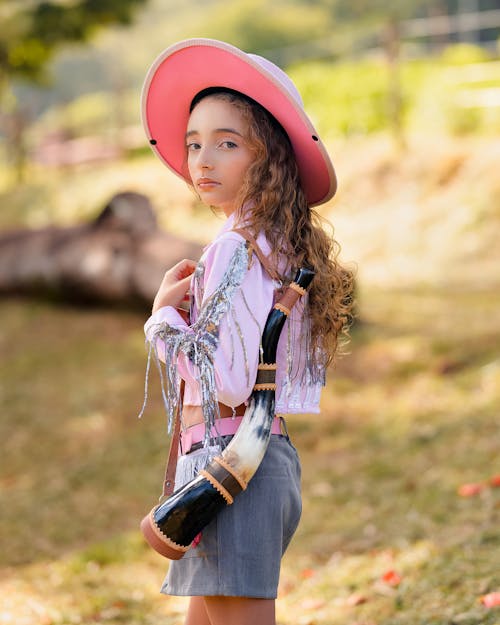 A little girl in a pink hat and pink shirt holding a guitar