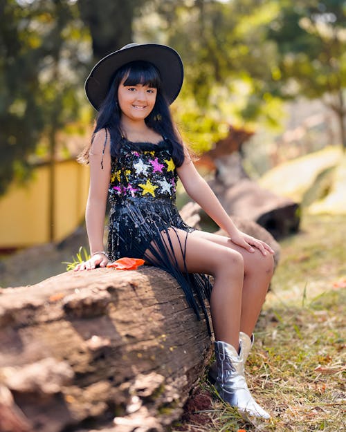 A girl in a hat and boots sitting on a log