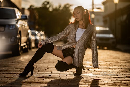 A woman in thigh high boots and a jacket posing on a brick road