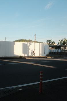 Shadow of a person walking along a white construction wall in an urban street environment.