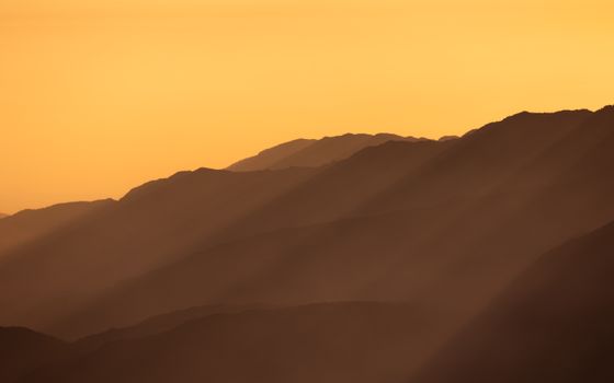 Peaceful view of distant mountain ranges with golden sunset hues casting long shadows.