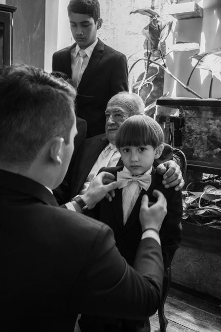 A classic black and white moment capturing a young boy being dressed in formal attire by family members.
