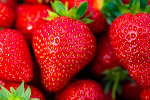 Free Macro shot of ripe red strawberries with green leaves, showcasing their vibrant color and texture. Stock Photo
