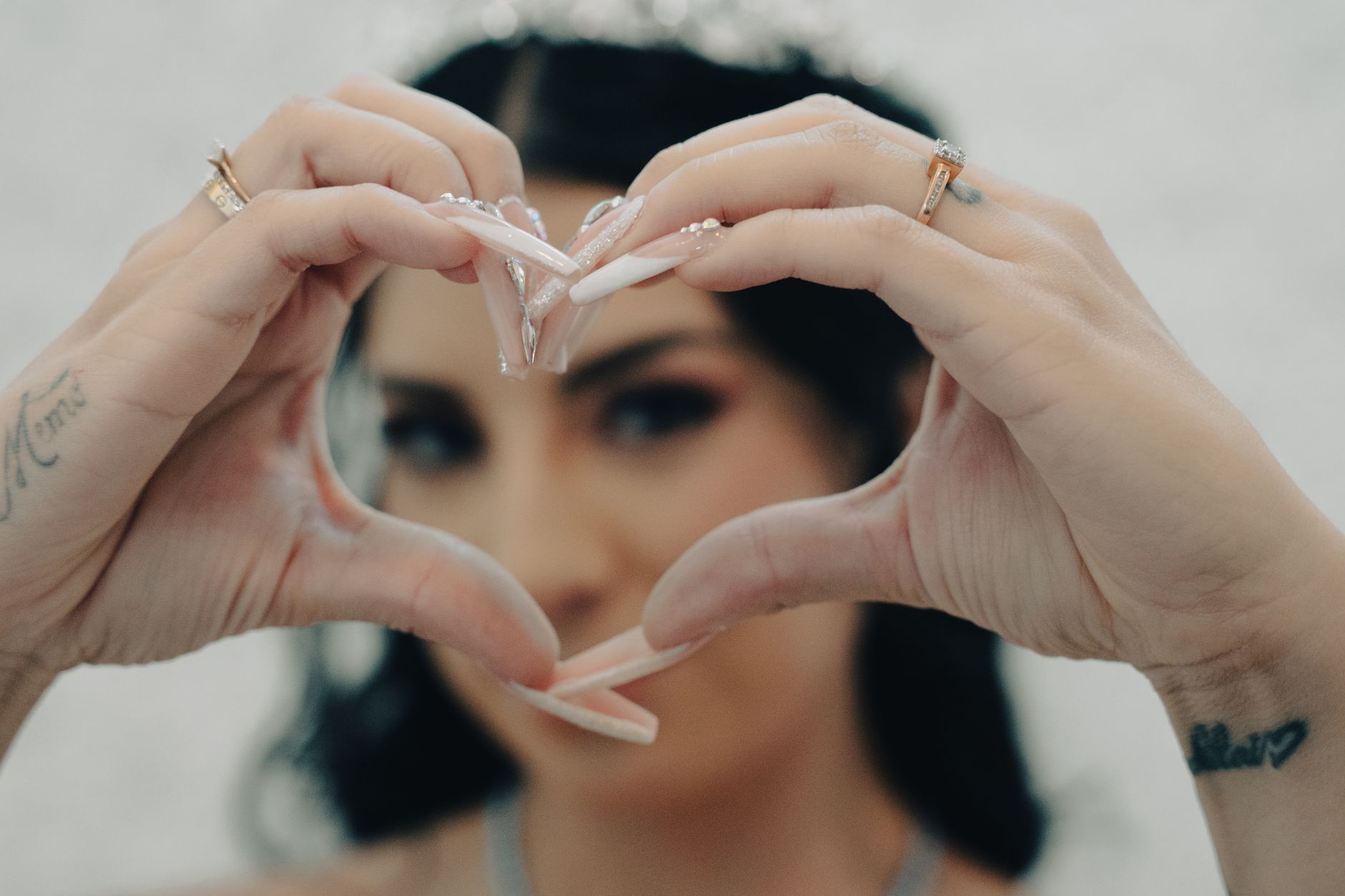 Hands forming a heart shape with tattoos and rings in focus, model blurred in background.