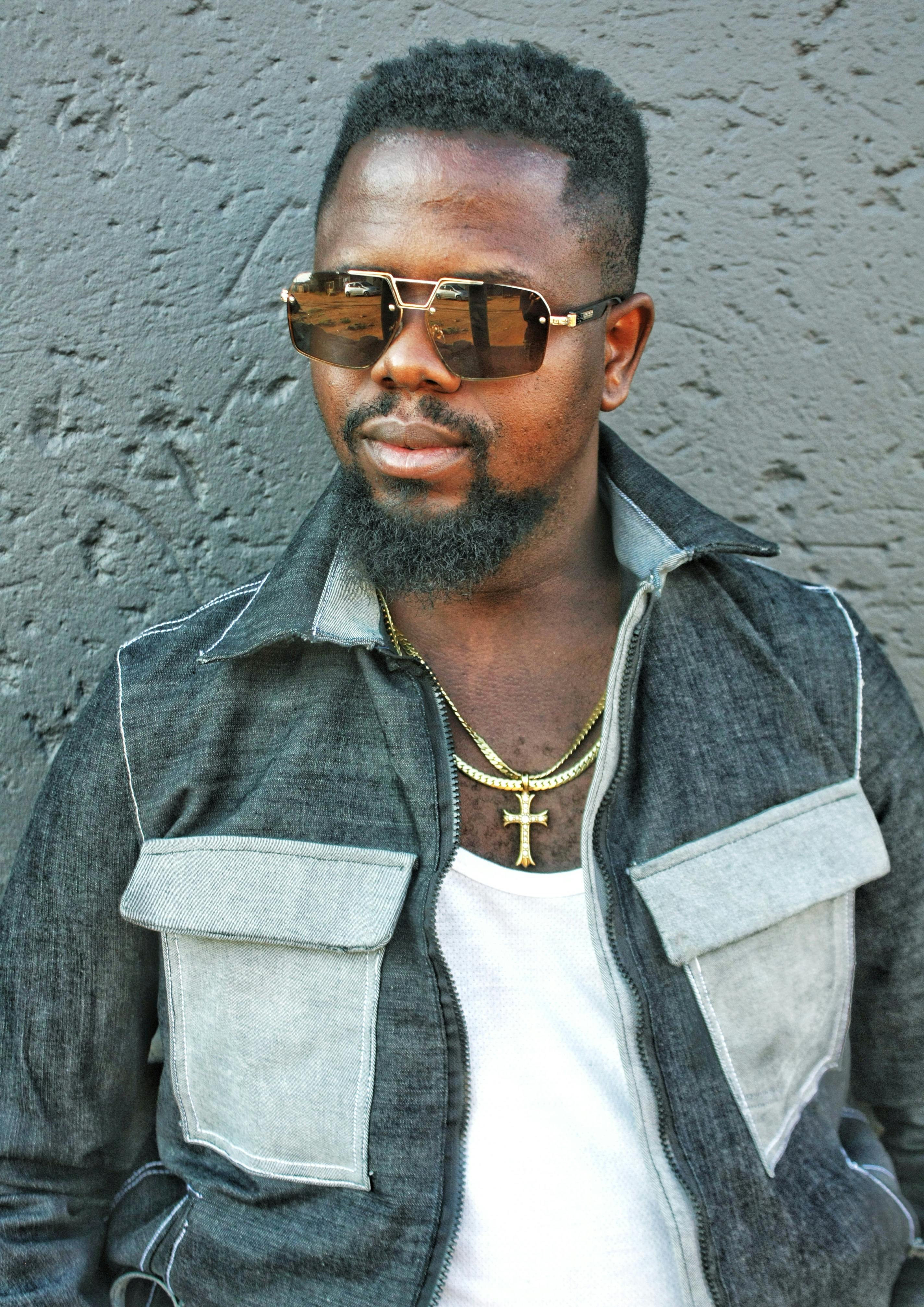 Portrait of a fashionable man with sunglasses and necklace against a gray background.