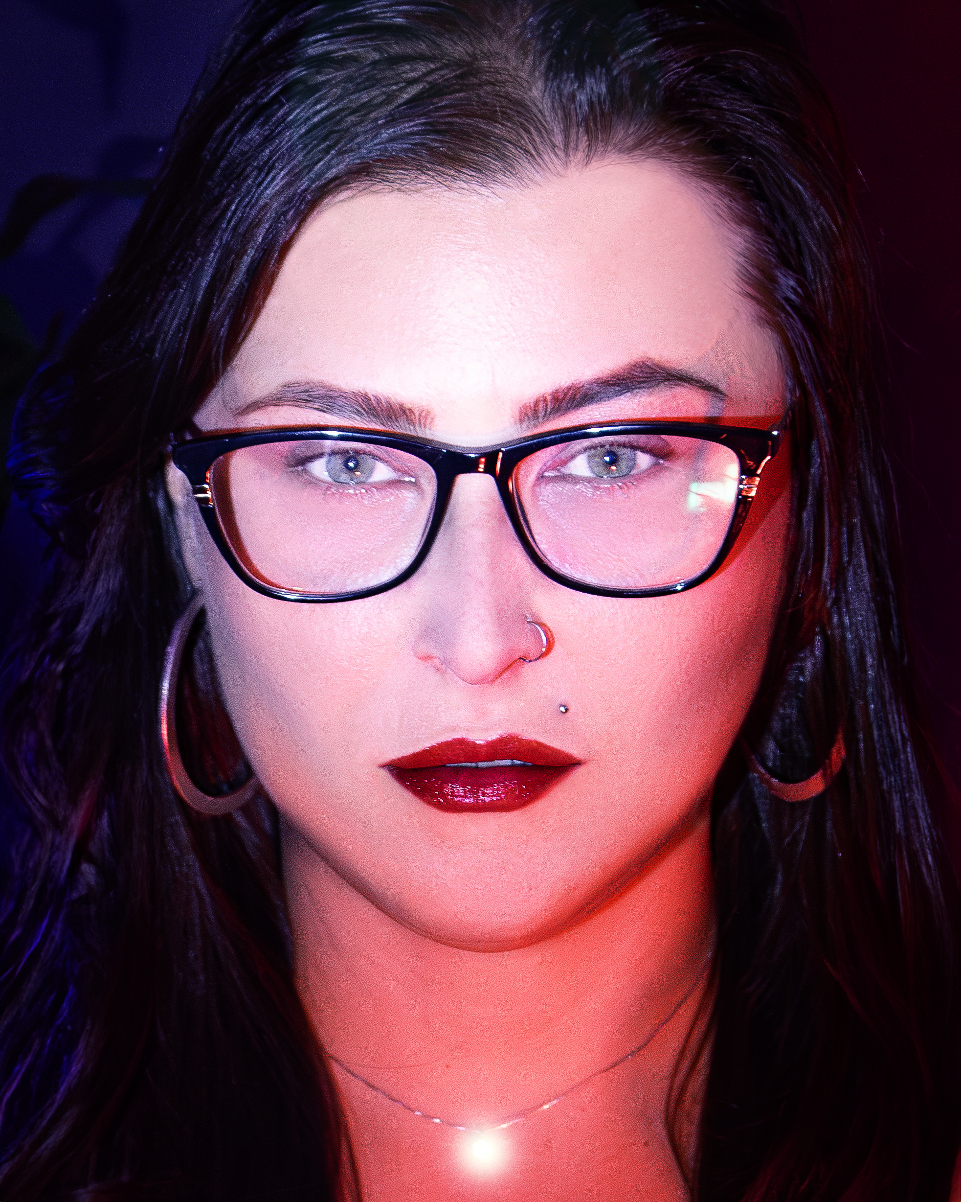 Close-up portrait of a stylish woman with eyeglasses and bold lipstick, featuring artistic lighting.