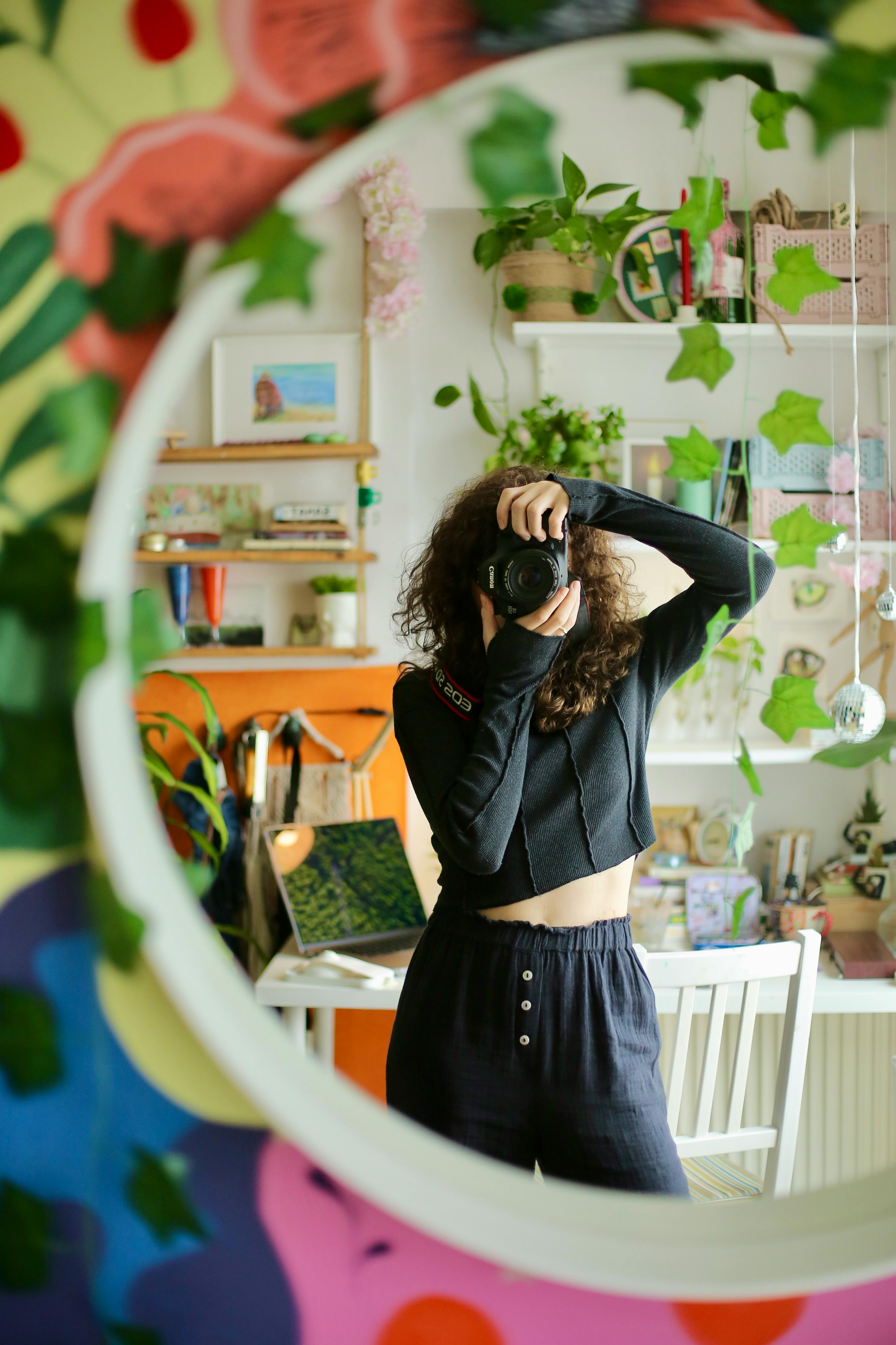 Artistic self-portrait of a woman taking a photo through a colorful mirror indoors.