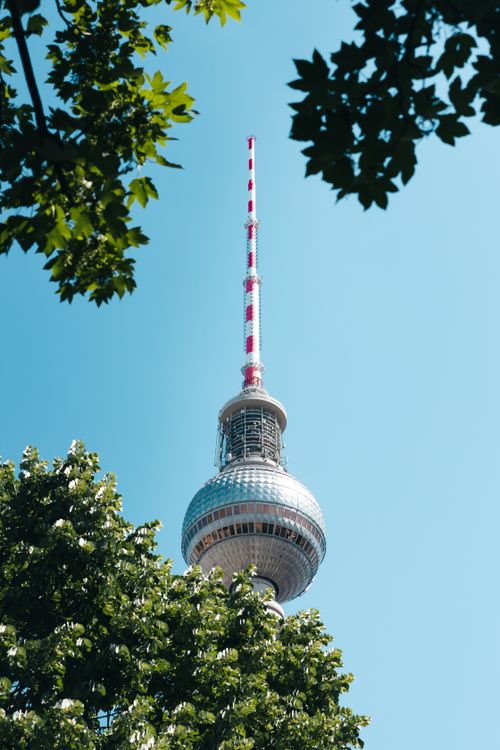 Free Iconic Berlin TV Tower framed by tree leaves against a clear blue sky. Stock Photo